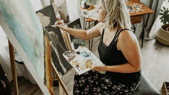 Illustrasjonsbilde av en kvinne som sitter og maler på et lerret.