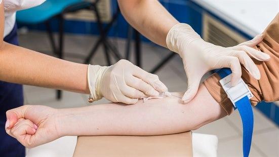 Fotoet viser blodprøvetaking. Bildeutsnittet viser armene til en helsearbeider ikledd engangshansker som tar en bloprøve på innsiden av albuen til en annen person.  