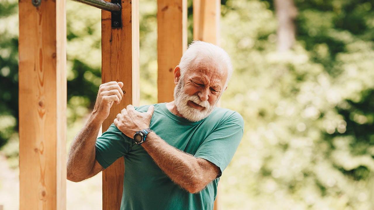 Illustrasjonsfoto av en eldre mann med hvitt hår og skjegg holder seg på skulderen og viser smerte. 