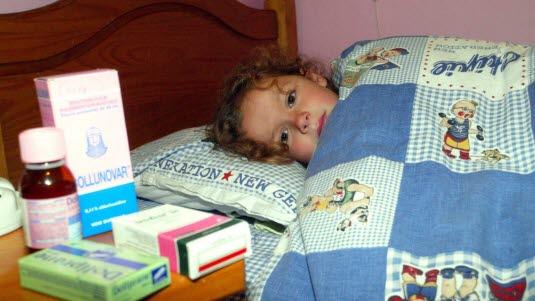 Et barn som ligger i sengen og som har flere typer medisin på nattbordet