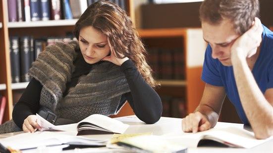 En kvinnelig og en mannlig student leser hver sin bok på en lesesal.