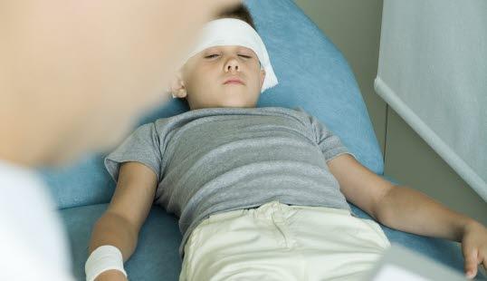 Et pbarn ligger i en sykeseng og har fått bandasje rundt hode