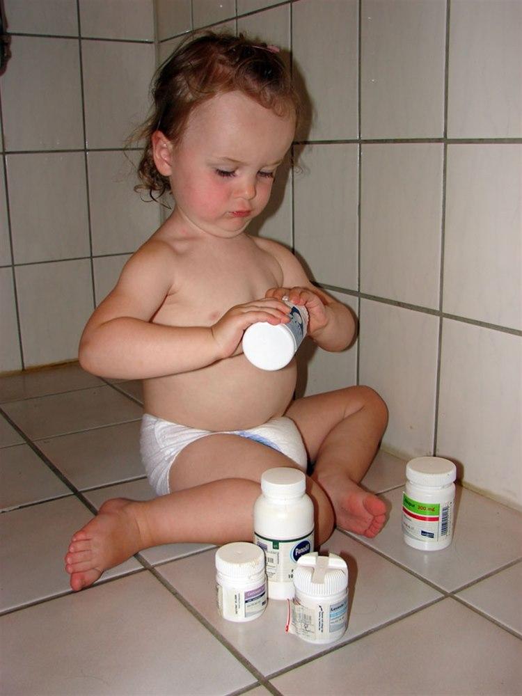 Et barn sitter på baderomsgulvet med flere tablettbeholdere og barnet er på vei til å åpne den ene beholderen.