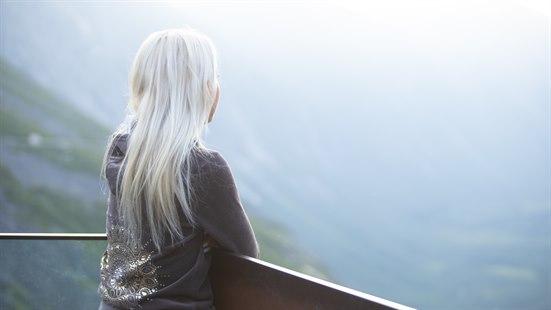 Illustrasjonsfoto av en kvinne med lyst hår som står og ser utover et landskap fra et utsiktspunkt.