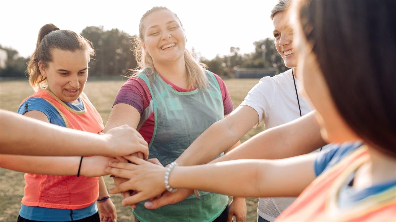 Illustrasjonsbildet viser en gruppe kvinner som er utendørs og trener. De står i ring med hendene i midten for heiarop.