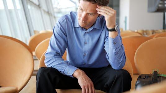 Man sitter på en stol i et lokale og holder ene hånden mot pannen