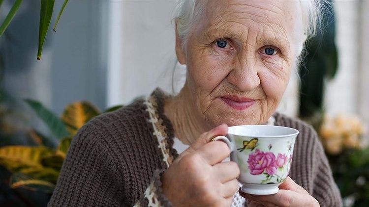 Nærbilde av en eldre dame som holder en kaffekopp i porselen