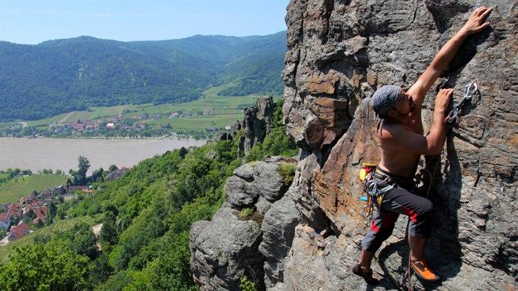 Illustrasjonsfoto: Ung mann i bar overkropp klatrer i en fjellvegg med vakker natur i bakgrunnen..