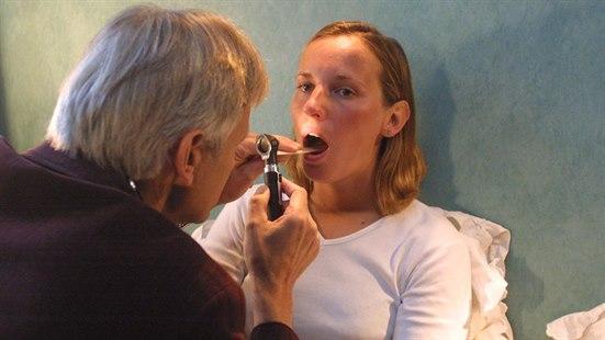 Lege undersøker munnen til en pasient med et otoskop og en munnpinne