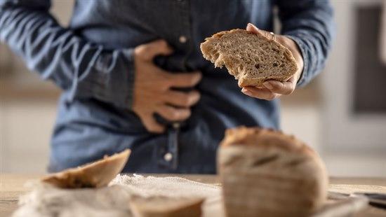 Person som spiser en brødskive og tar seg til magen som uttrykk for magesmerter.