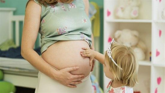 Illustrasjonsfotoet viser en gravid mage og et barn som holder på kvinnens mage