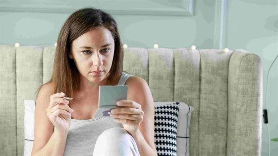 Illustrasjonsfoto: Ung kvinne sitter i sengen. Holder i en pinsett og ser seg i et lommespeil.