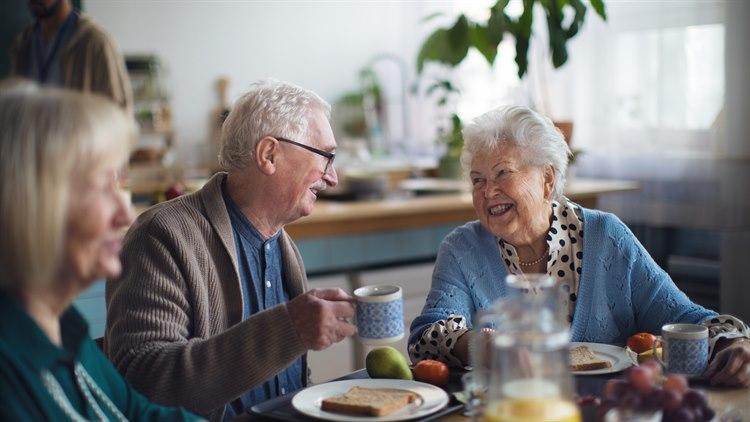 Illustrasjonsfoto av tre eldre mennesker som sitter rundt et bord og har et hyggelig måltid sammen.