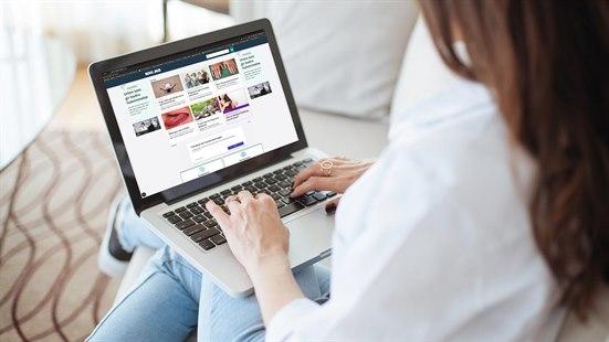 Illustrasjonsfoto av kvinne som sitter komfortabelt i en sofa med laptop i fanget. Skjermen viser at hun utforsker forsiden av NHI.no.