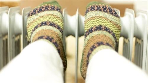 Illustrasjonsfoto: Føtter med fargerike ullsokker som hviler på en radiator.
