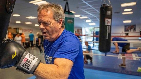 Mann med boksehansker bokser mot en sekk i en boksesal.