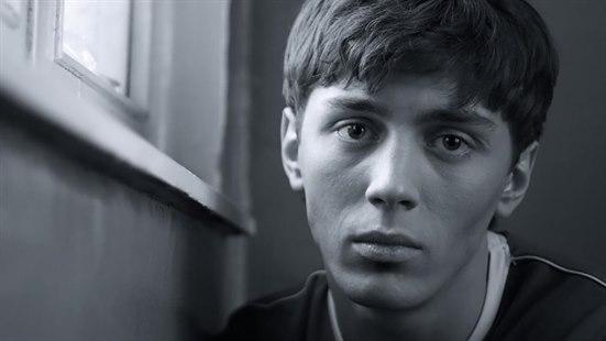 Illustrasjonsfoto i svart-hvit av en ung gutt som sitter ved siden av et vindu. Gutten har et tomt blikk rettet mot  oss.