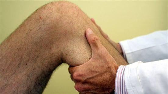 Behandler som undersøker kne til en mannlig pasient