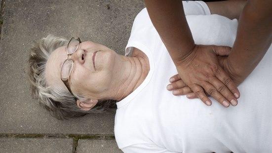Nærbilde av en eldre dame som ligger på gaten og som får utført brystkompresjon