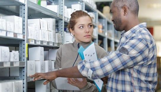 Mann og kvinne diskuterer foran lager av legemidler