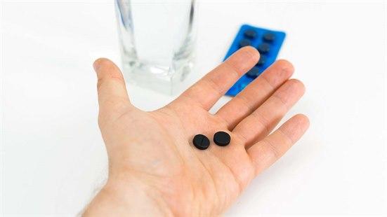 Nærbilde av en håndflate med to svarte tabletter og i bakgrunnen ser vi flere tabletter og et vannglass.