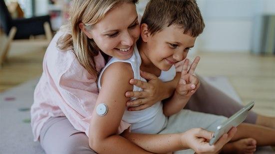Illustrasjonsfoto av en gutt med diabetes som sitter sammen med sin mor - som holder rundt han. Begge smiler. 