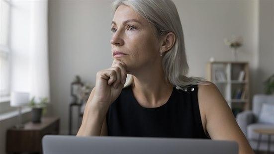 Illustrasjonsfoto av en voksen dame som ser tankefullt ut i rommet med hun sitter foran sin pc
