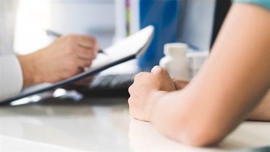 Illustrasjonsfotoet viser en lege og en pasient på et behandlerkontor. Fotoet viser kun hender og armer, og legen noterer på en notatblokk