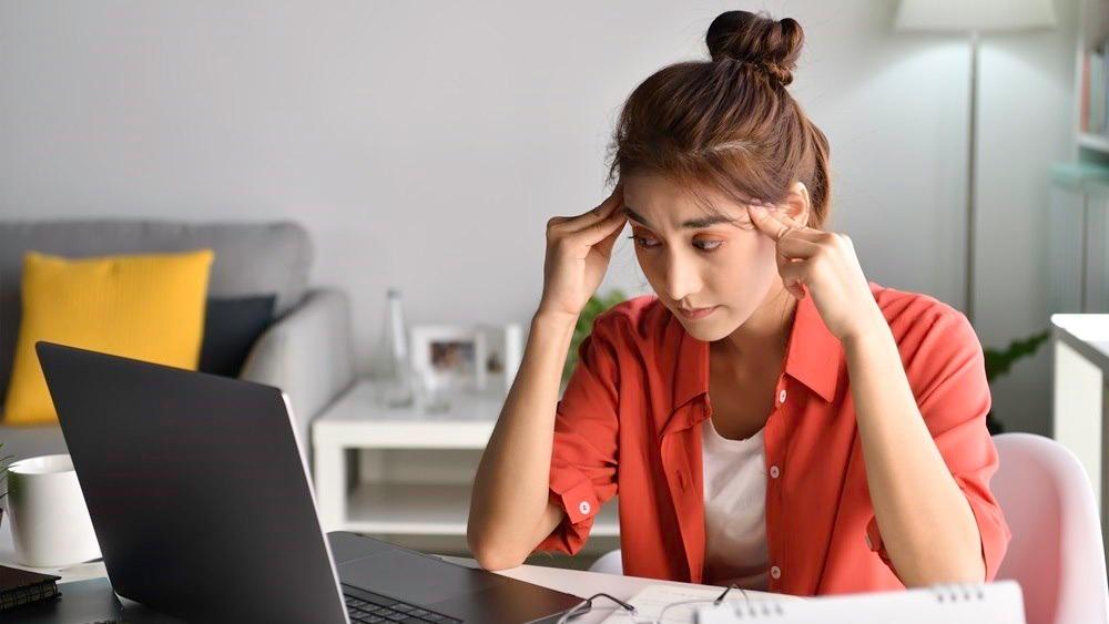 Ung kvinne som tar seg til tinningene samtidig som ser på en skjerm. Tydelig ubehag.