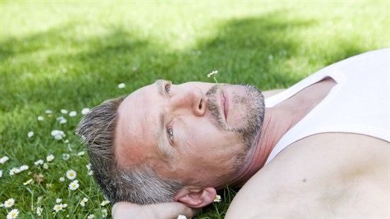 Illustrasjonsfoto av en mann som ligger i gresset med en blomst (tusenfryd) i munnen.