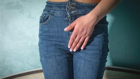 Illustrasjonsfotoet viser nærbilde av en kvinne fra livet og ned til lårene. Hun er kledd i jeans og holder seg foran skrittet med en hånd.