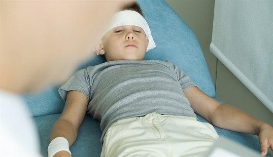 Et pbarn ligger i en sykeseng og har fått bandasje rundt hode