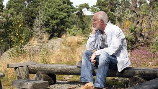 Eldre mann sitter ute på en benk og støtter tankefult hodet i hånden