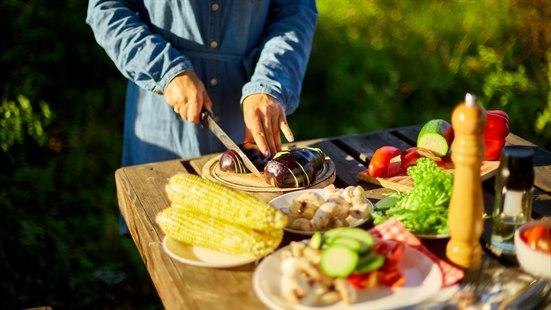 Illustrasjonsfoto av en person som skjærer løk ute ved et bord fullt av mat.