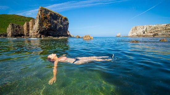Illustrasjonfoto av kvinne som flyter på ryggen i sjøen i fint vær.