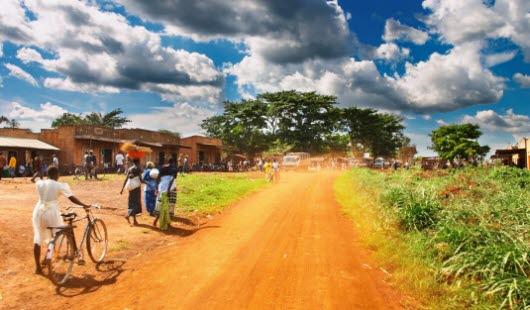 Illustrasjonsfotoet viser afriansk landsby. Vi ser mennesker ved husene og langs veien.