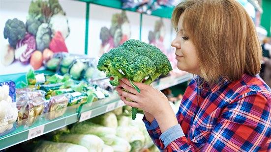 Illustrasjonsfoto av en dame som er på butikken og holder en brokkoli mellom hendene som hun lukter på. 