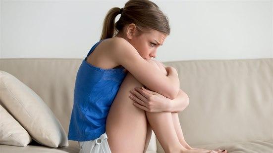 Illustrasjonsfoto av en kvinne som sitter i fosterstilling i sofaen. Kvinnen ser bekymret ut.