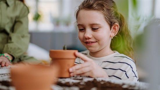 Smilende jente ser at det gror fra en liten keramikkpotte.