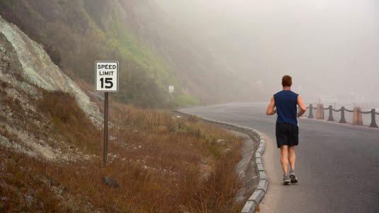 Illustrasjonsfoto av en ung mann som løper på veien, med fjell på venstre side og en sving foran løperen.