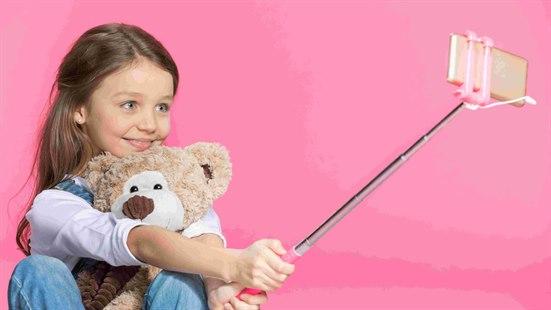 Illustrasjonsfoto: Poserende jente med teddybjørn og smarttelefon i selfiestang.