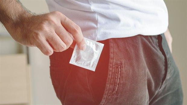 Illustrasjonsfotoet viser nærbilde av bekkenområdet til en mann som holder en kondom foran bukselommen