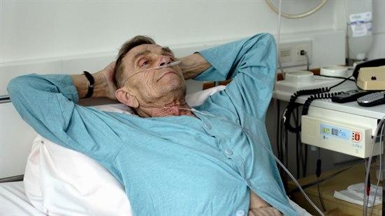 Eldre pasient ligger i sykehusseng og får oksygentilførsel via nesen.