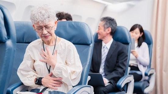 Illustrasjonsfoto av en eldre dame som sitter i flysetet, og holder seg over brystet og magen. Hun ser uvel ut.