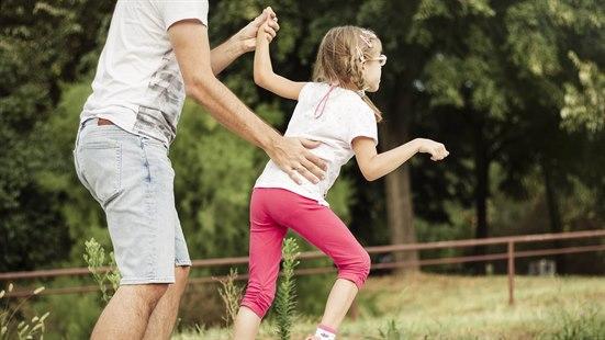 Illustrasjonsfoto av ei jente med cerebral parese. Hun går i parken med sin far som holder hånden hennes og støtter den andre hånden på ryggen hennes.
