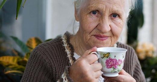 Nærbilde av en eldre dame som holder en kaffekopp i porselen