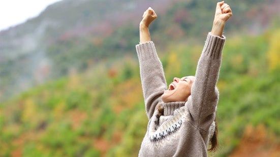 Illustrasjonsfoto av en dame er i naturen og jubler med hendene i været.