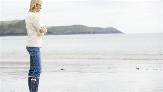 En kvinne står i strandkanten og ser utover sjøen.