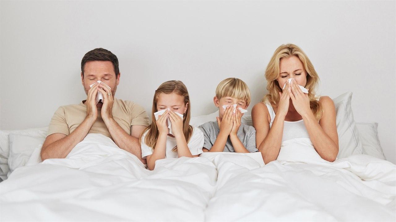 Illustrasjonsfotoet viser en familie som ligger syke i sengen. De er forkjølet, og alle snyter nesene med papirlommetørkle samtidig. 