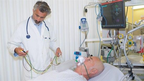 Lege står ved sengen til en sengeliggende syk pasient.